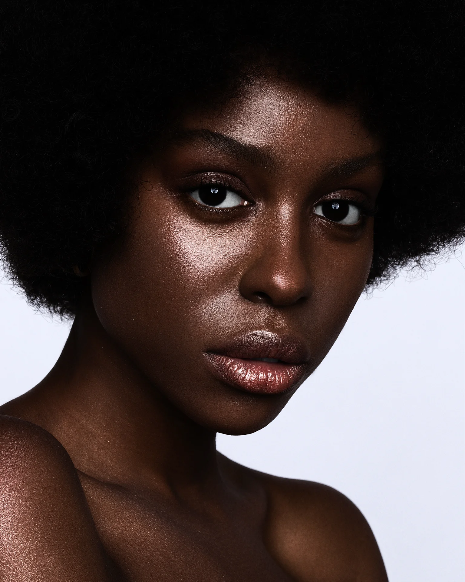 Retouched beauty portrait of a model with dark skin, featuring dodge and burn, deep color grading, and strictly preserved natural skin texture, photography by Iulia David