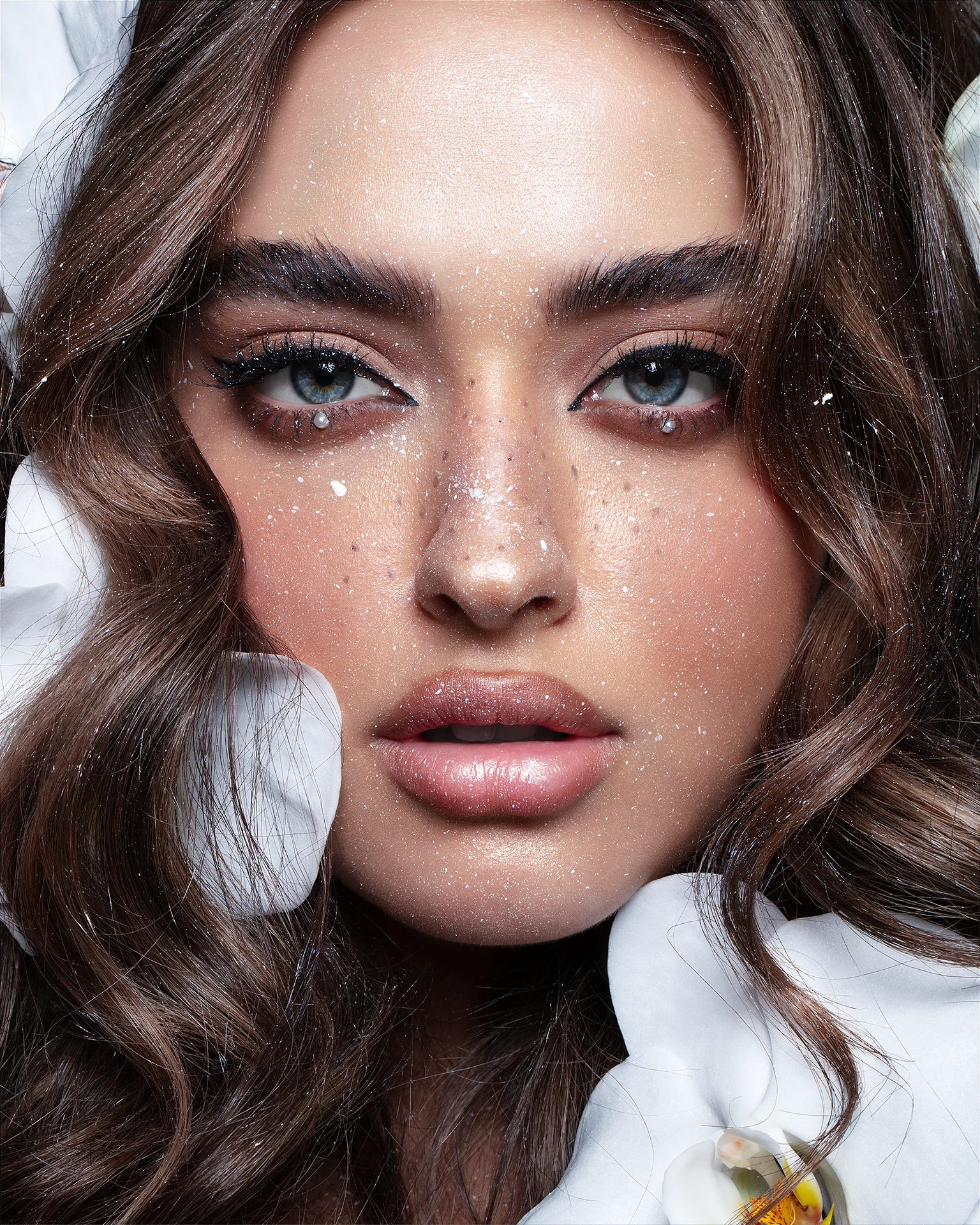 Close-up beauty portrait retouching of a model with orchid petals and glitter details, featuring dodge and burn, skin texture preservation, and color grading, photography by Abu Haye