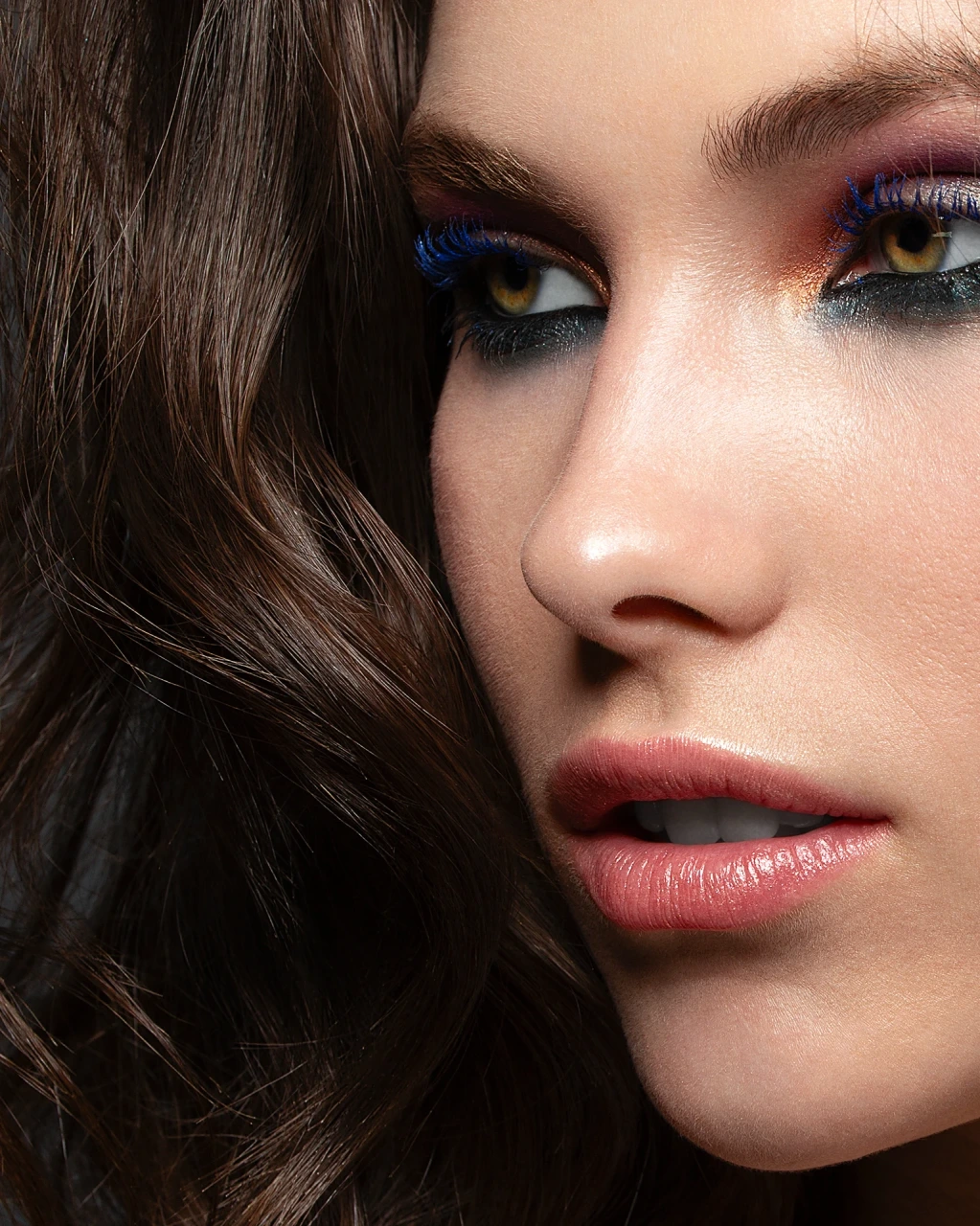 Commercial beauty portrait close up with electric blue mascara, bronze eyeshadow and glossy lips, high-end skin texture retouching and hair cleanup